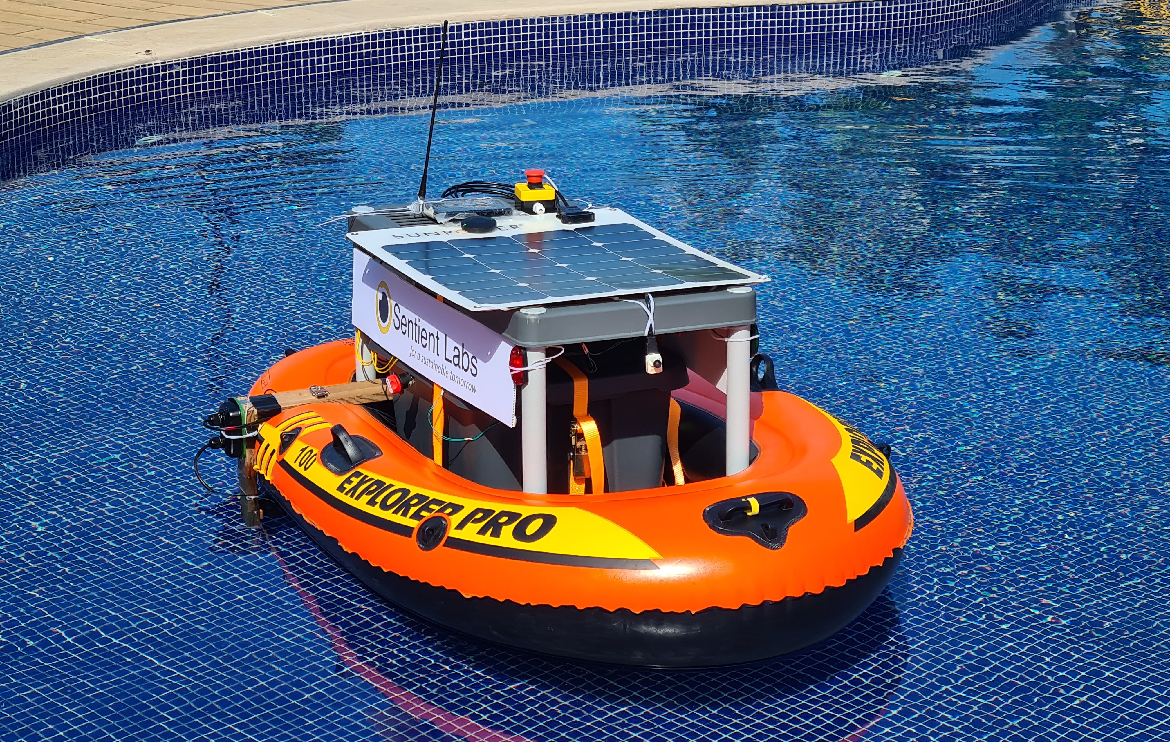 The Sentient Labs USV prototype under test in a pool: an inflatable hull carrying a solar panel, radio antenna, emergency stop and thruster.